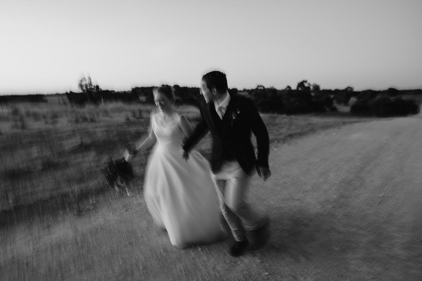 A bride and groom running down a dirt road enjoying themselves.