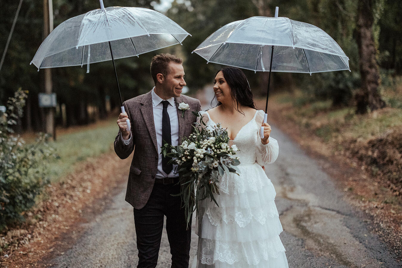 A bride and groom holding umbrellas keeping dry on their rainy wedding day.