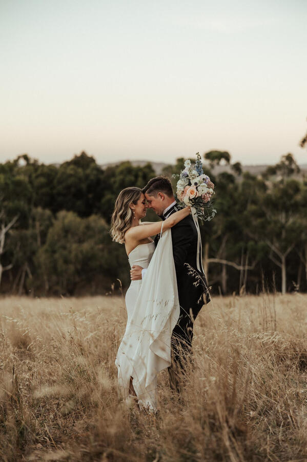 A bride and groom embrace in a field at Nether Hill Farm in the Adelaide Hills at sunset.
